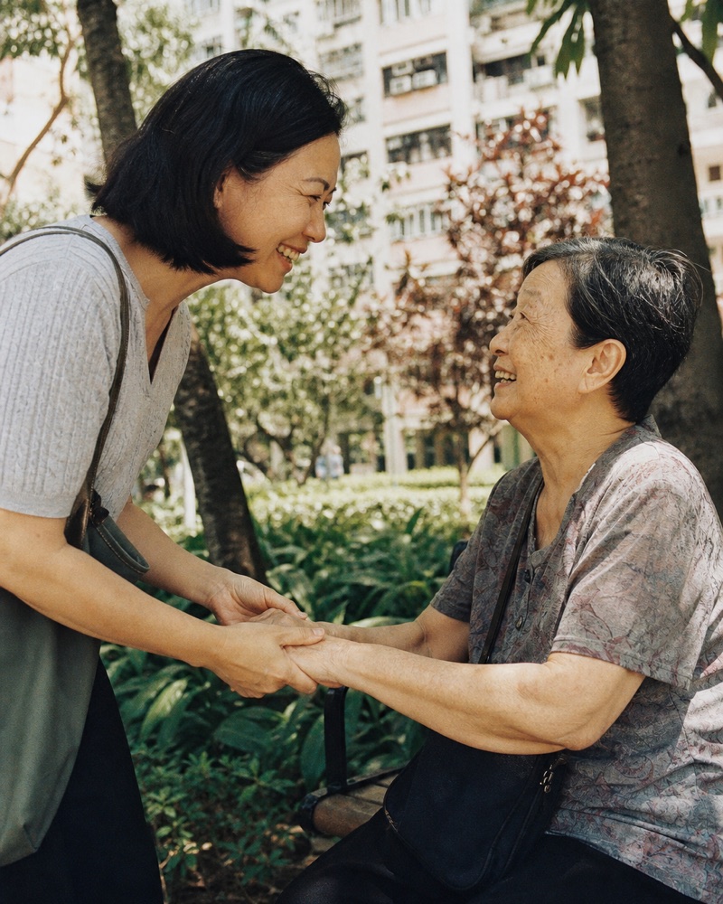 A Chinese adult daughter warmly greeting her elderly mother in a sunny garden