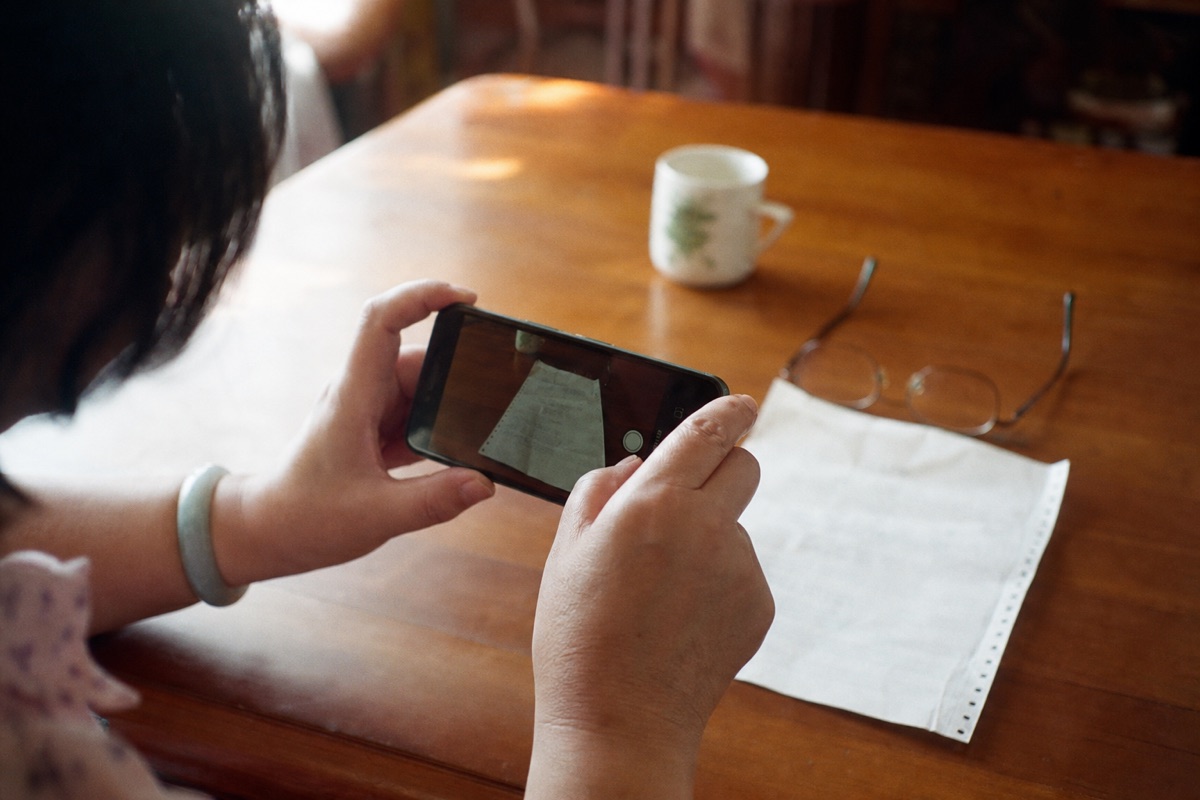 Hands holding a smartphone to photograph a paper document on a wooden table