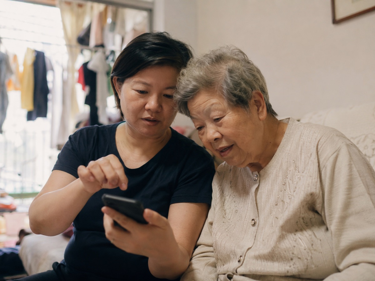 A Chinese adult daughter showing her elderly mother how to use a smartphone on a sofa